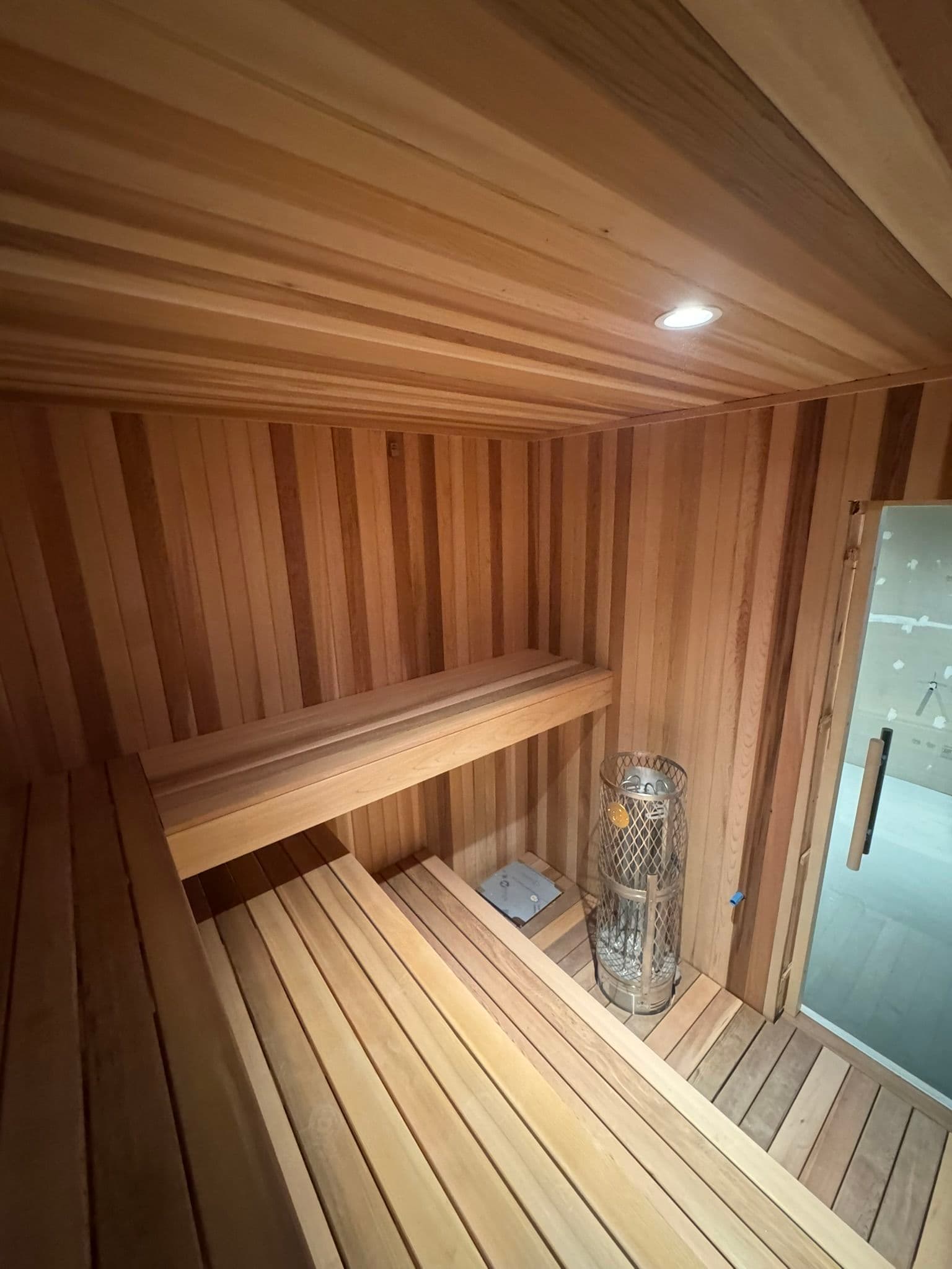 Interior of a wooden sauna featuring cedar planks, benches, and a heater. Relaxation space.