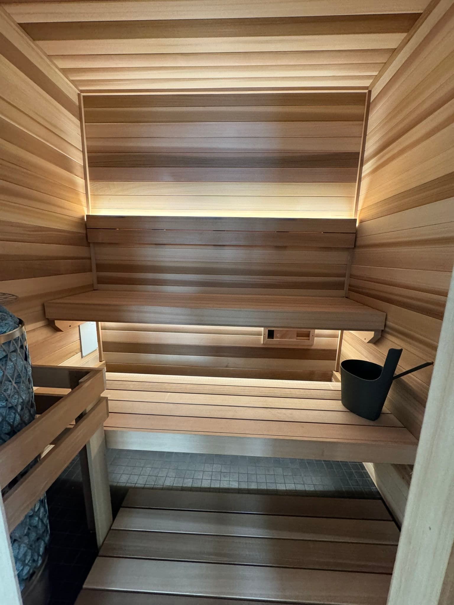Cozy wooden sauna interior with benches, soft lighting, and a bucket for water.