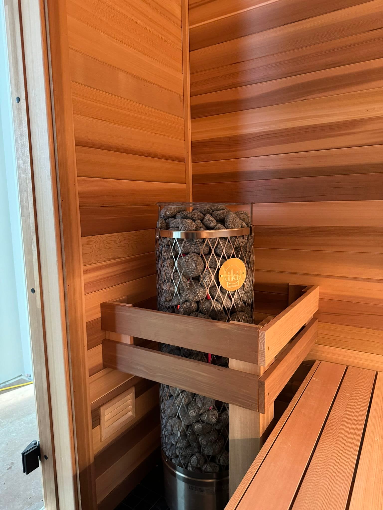 Wooden sauna interior with a metal stove filled with heated rocks and seating area.