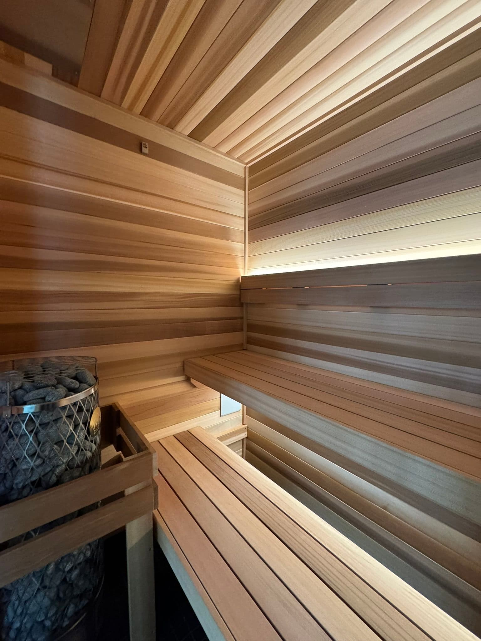 Inside a wooden sauna with benches, soft lighting, and stones for heating. Relaxation space.