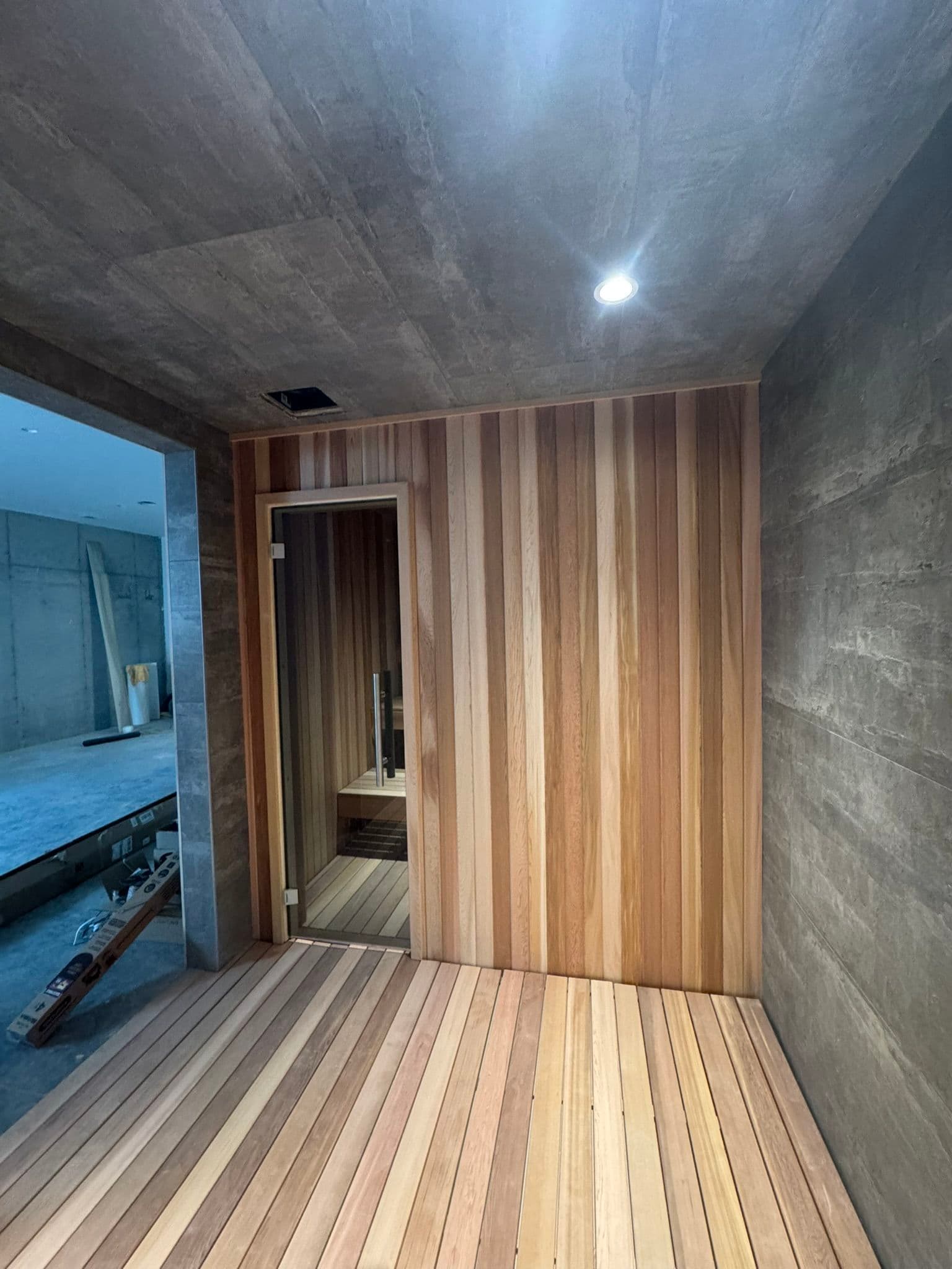 Modern sauna interior with wooden slats and concrete wall, featuring soft LED lighting.