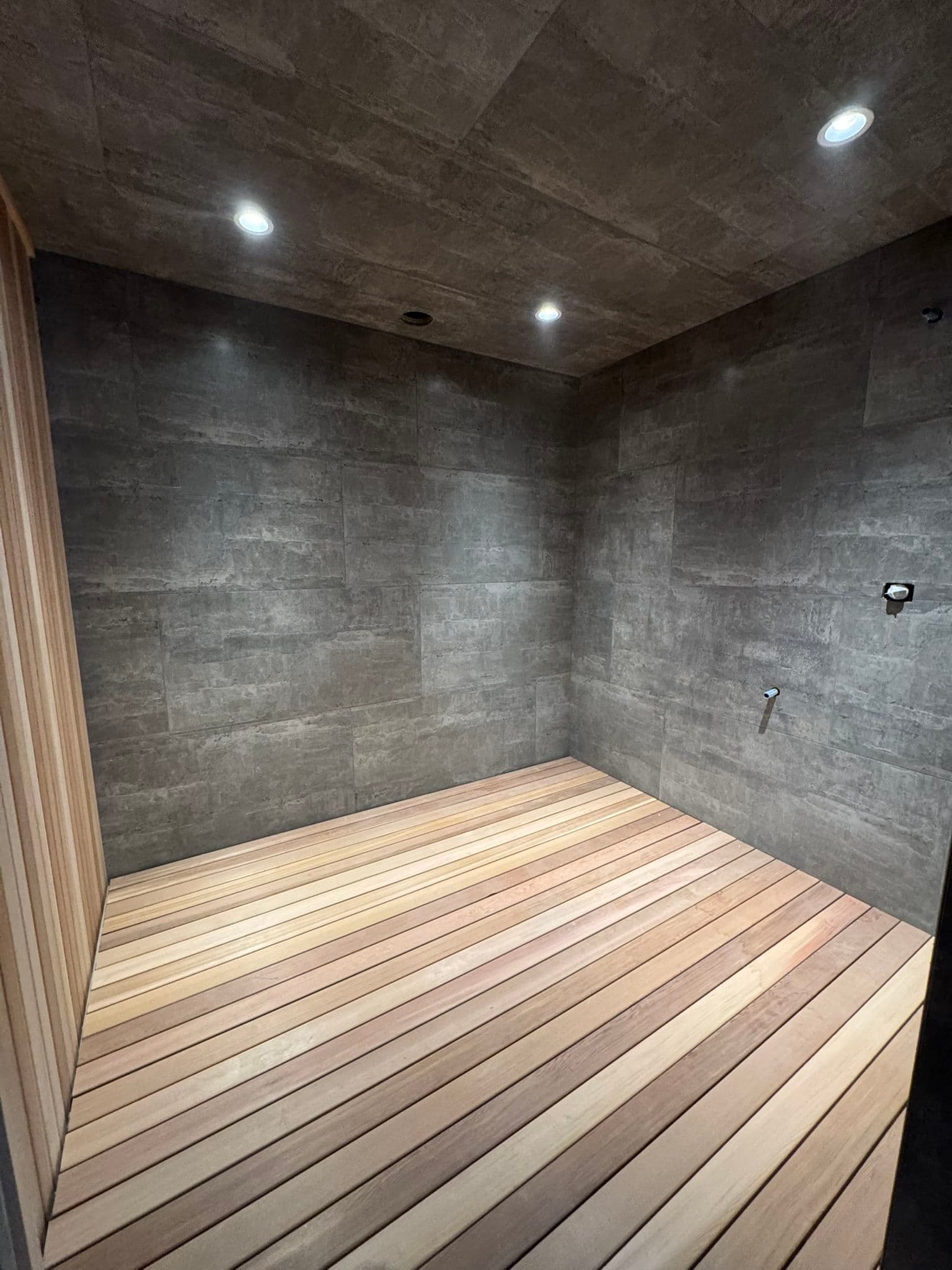 Modern shower space with wooden slatted flooring and stone textured walls, well-lit design.